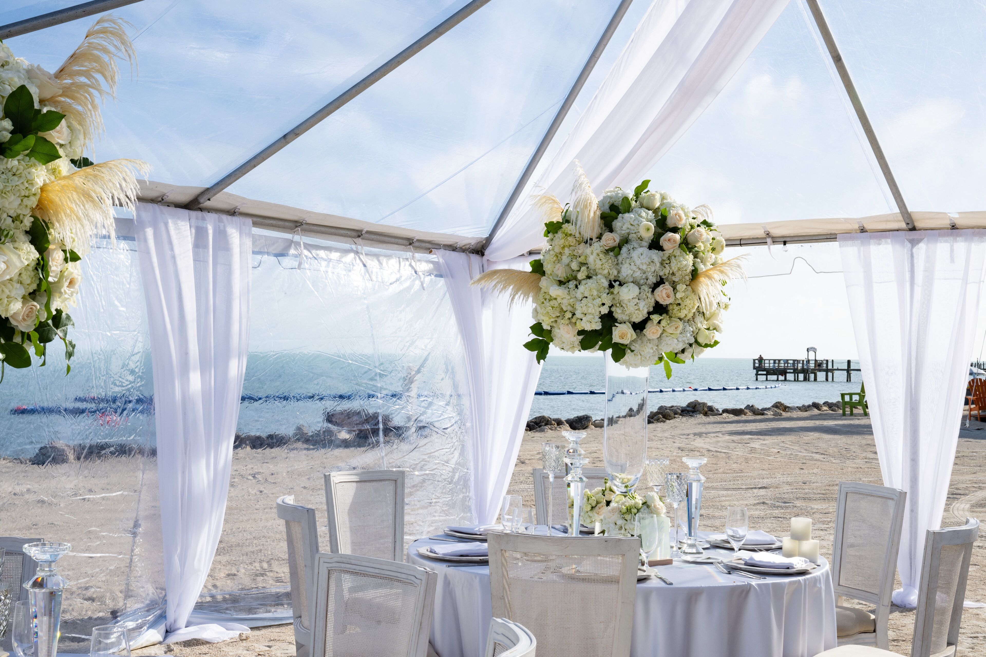 A tented wedding setup with white drapery, floral arrangements, and tables set for a reception.
