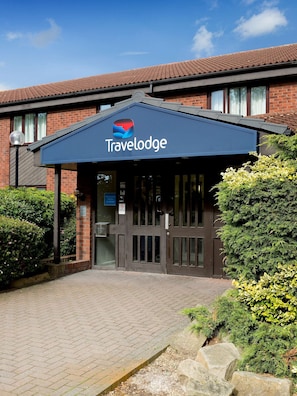 A Travelodge hotel entrance with a dark blue awning, brick facade, and a clear sky. - Travelodge Nuneaton Bedworth (Nuneaton)
