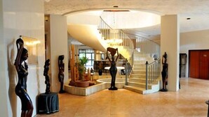 A spacious lobby with a grand staircase, a central art display, and a modern light fixture. - Mariador Palace (Conakry)