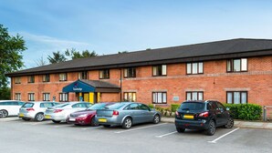 A Travelodge hotel with a brick facade, multiple parking spaces, and a blue awning. - Travelodge Dumfries (Dumfries)