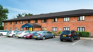 A Travelodge hotel with a brick facade, multiple parking spaces, and a clear blue sky. - Travelodge Dumfries (Dumfries)