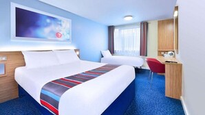 A hotel room with a large bed, a smaller bed, a desk with a chair, a TV mounted on the wall, and a window with curtains. - Travelodge Dumfries (Dumfries)
