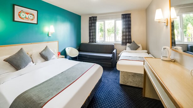 A hotel room with a bed, a sofa, a desk, and a window with curtains. - OYO Sunrise Hotel, A46 N Leicester (Leicester)