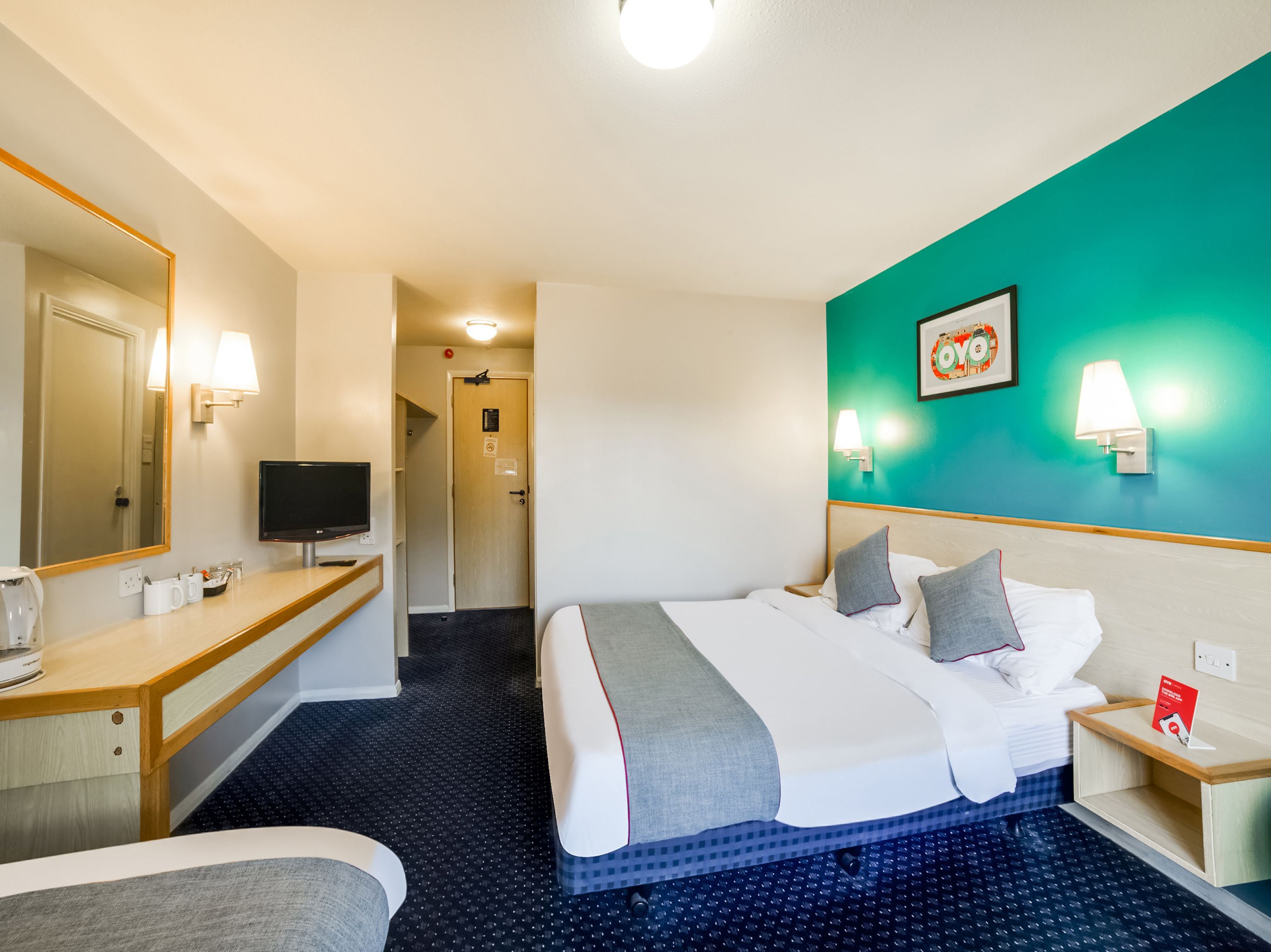 A hotel room with a bed, bedside table, TV, and a bathroom visible in the background.