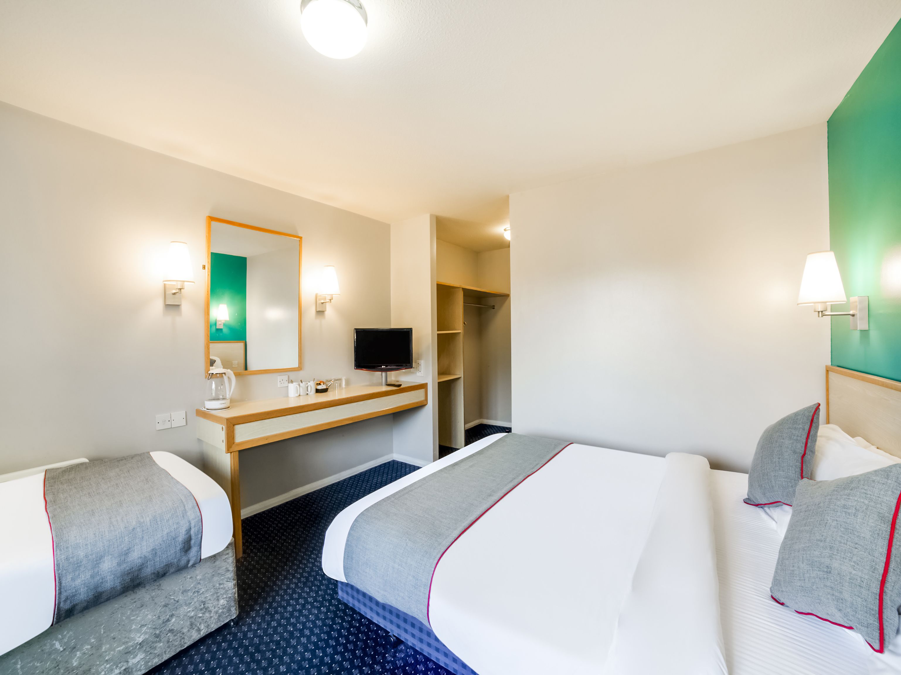 A hotel room with two beds, a desk with a TV, a mirror, and a wardrobe.