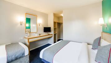 A hotel room with two beds, a desk with a TV, a mirror, and a wardrobe.
