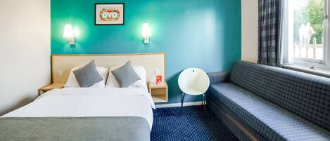 A hotel room with a bed, a seating area, and a window with curtains.