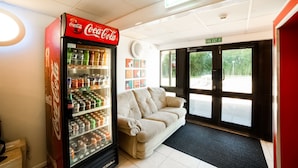 A Coca-Cola vending machine, a beige sofa, and a fire exit sign in a lobby area. - OYO Sunrise Hotel, A46 N Leicester (Leicester)