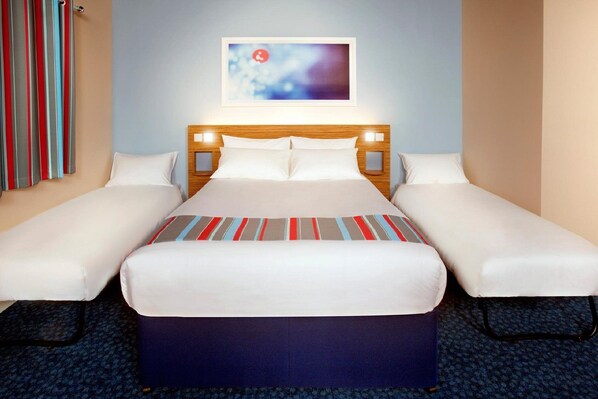 Quarto de hotel com uma cama grande, duas camas de solteiro, cabeceira de madeira, quadro emoldurado na parede e carpete estampado.