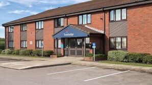 A Travelodge hotel with a brick facade, a blue awning, and a parking lot. - Travelodge Grantham South Witham (Grantham)