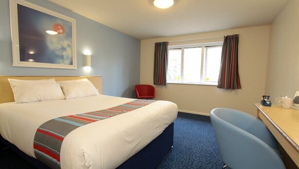 A hotel room with a bed, a desk, a chair, a window with curtains, and a painting on the wall. - Travelodge Grantham South Witham (Grantham)