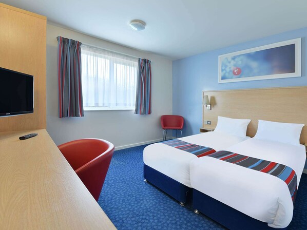 A hotel room with a bed, a desk with a TV, a red chair, and a window with curtains. - Travelodge Stirling M80 (Stirling)