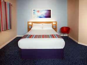 A hotel room with a bed, a red chair, a painting on the wall, and a striped curtain.