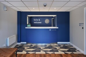 A reception area with a blue wall, a clock, and a 'hello & welcome' sign. - Travelodge Park Royal (London)
