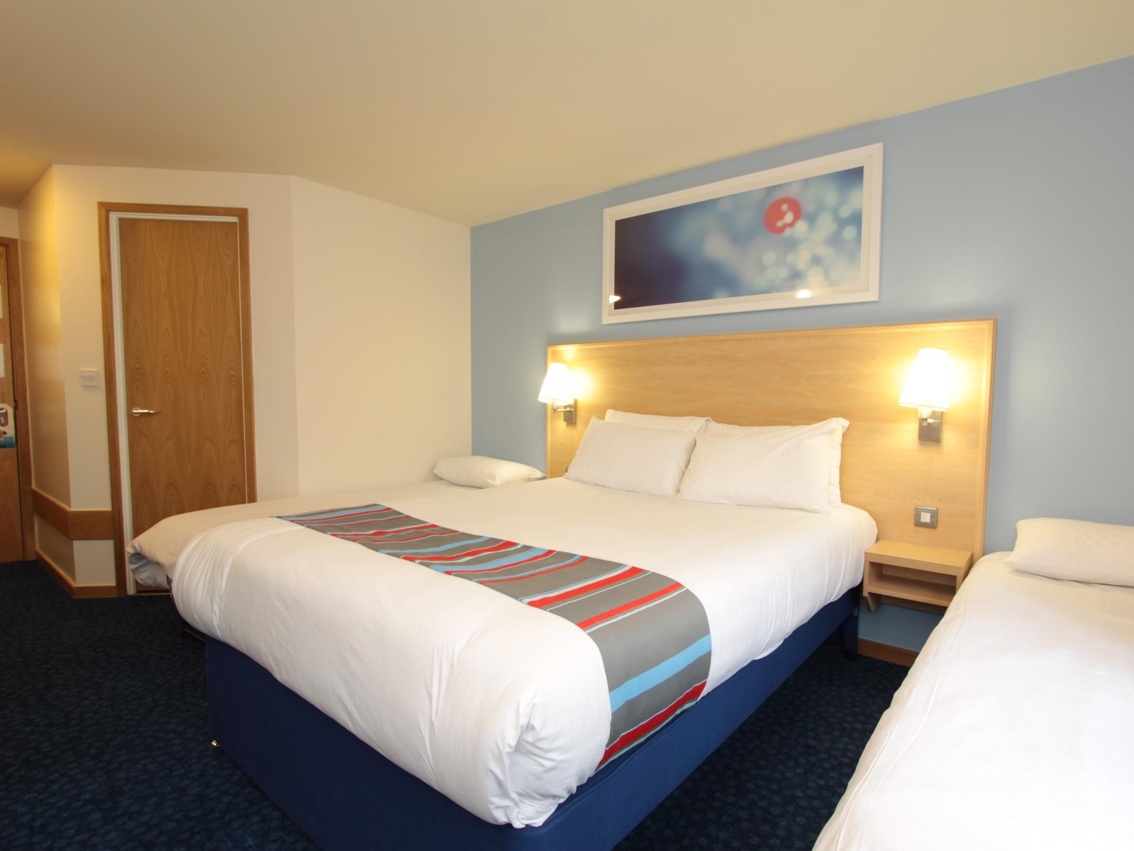A hotel room with a large bed, two bedside tables, a headboard, and a wall-mounted artwork.