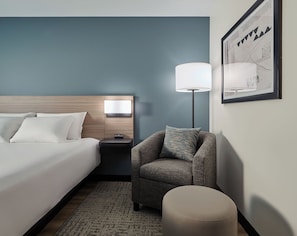 A hotel room with a bed, a nightstand, a lamp, a chair, and a rug.