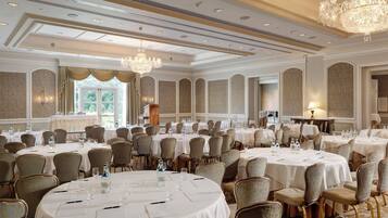 A banquet hall with round tables, chairs, and chandeliers.