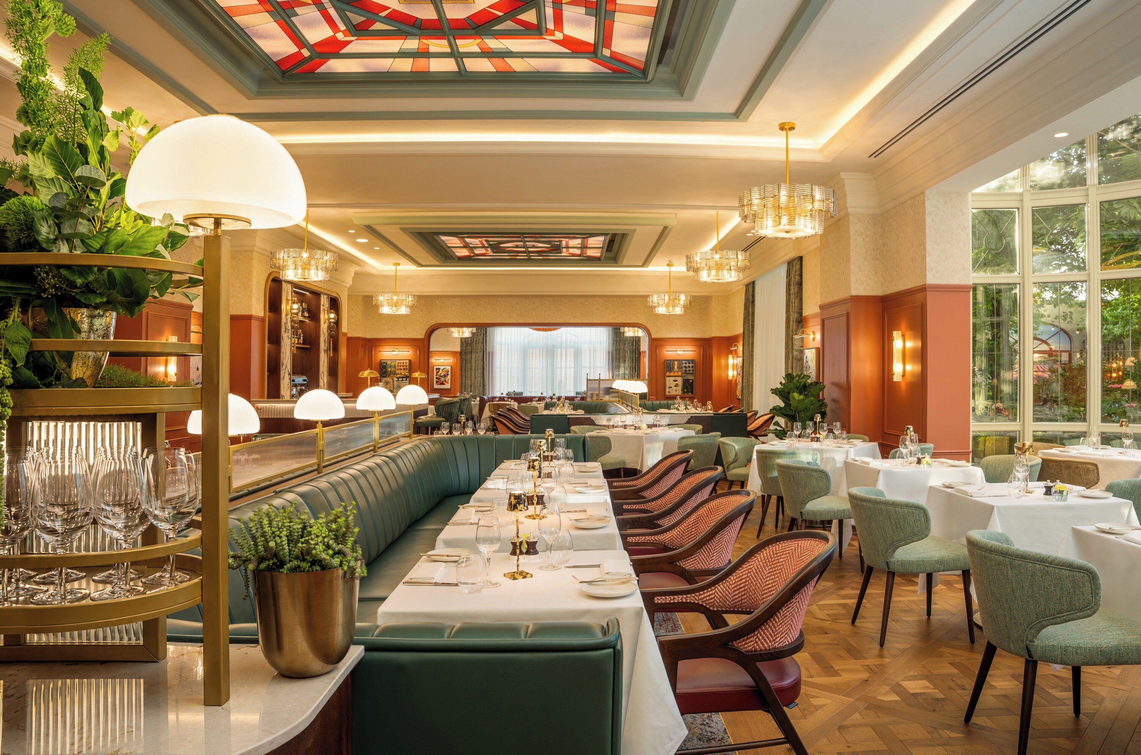 A restaurant with a long dining table, multiple chairs, and a high ceiling with a stained glass design.