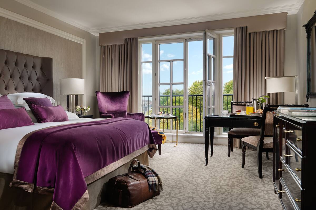 A hotel room with a large bed, a desk, a chair, and a view of the outdoors.