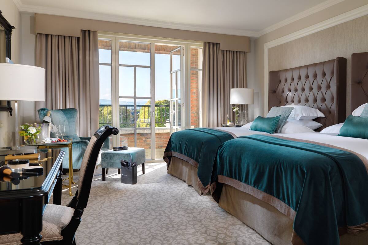 A hotel room with a large bed, two bedside tables, a desk with a chair, and a view of the outdoors.
