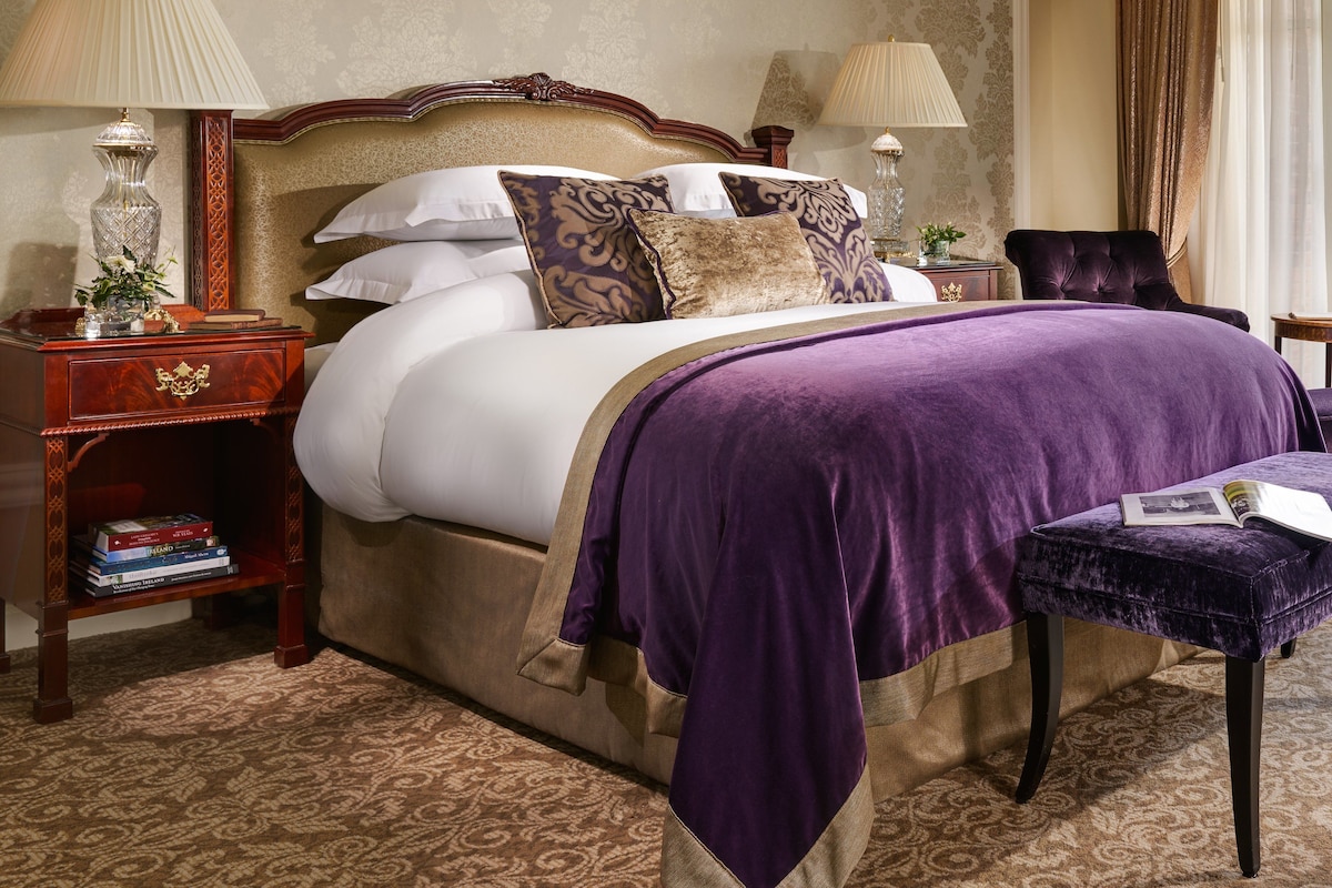 A well-appointed bedroom with a large bed, two bedside tables with lamps, a chair, and a small table with a book.