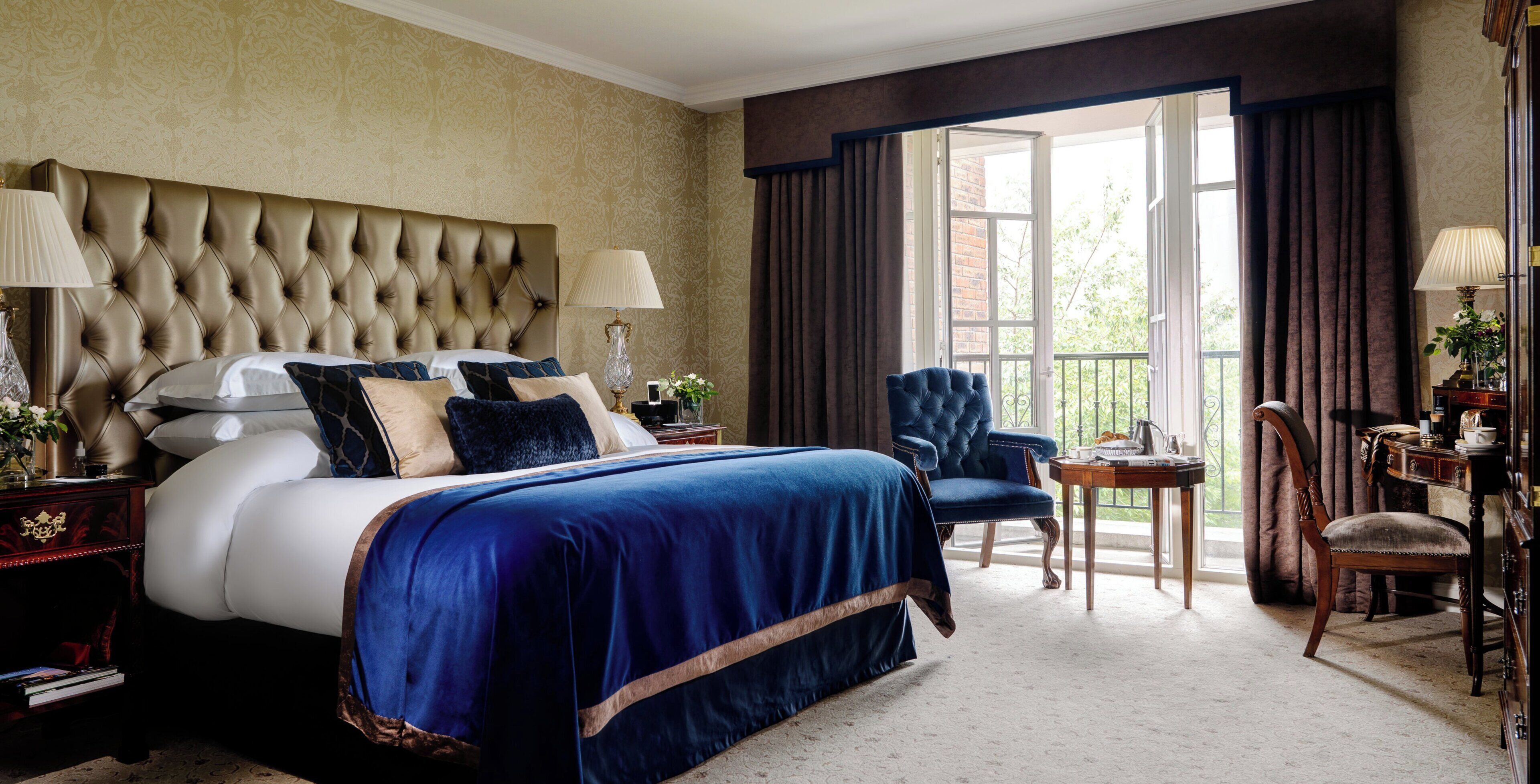 A well-appointed bedroom with a large bed, a sitting area with a chair, and a view through a window.