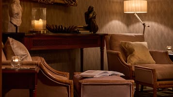 A room with a wooden table, two armchairs, a lamp, a statue, and a mirror.