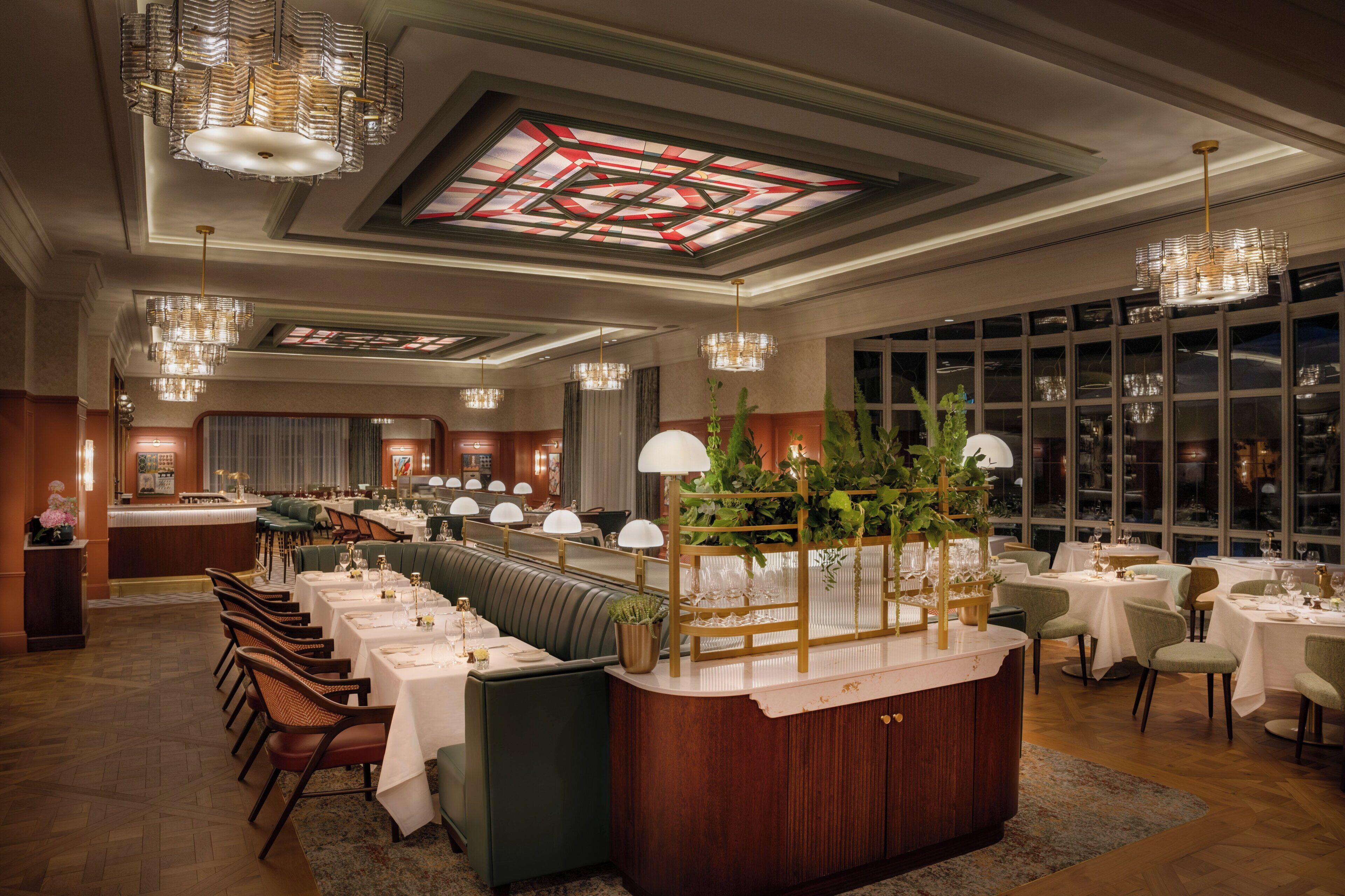 A restaurant with a long counter, multiple tables, and hanging chandeliers.