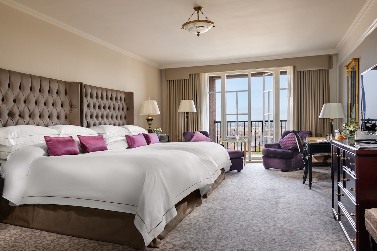 Une chambre d’hôtel avec un grand lit, deux tables de chevet, un bureau, une chaise et un balcon avec vue.