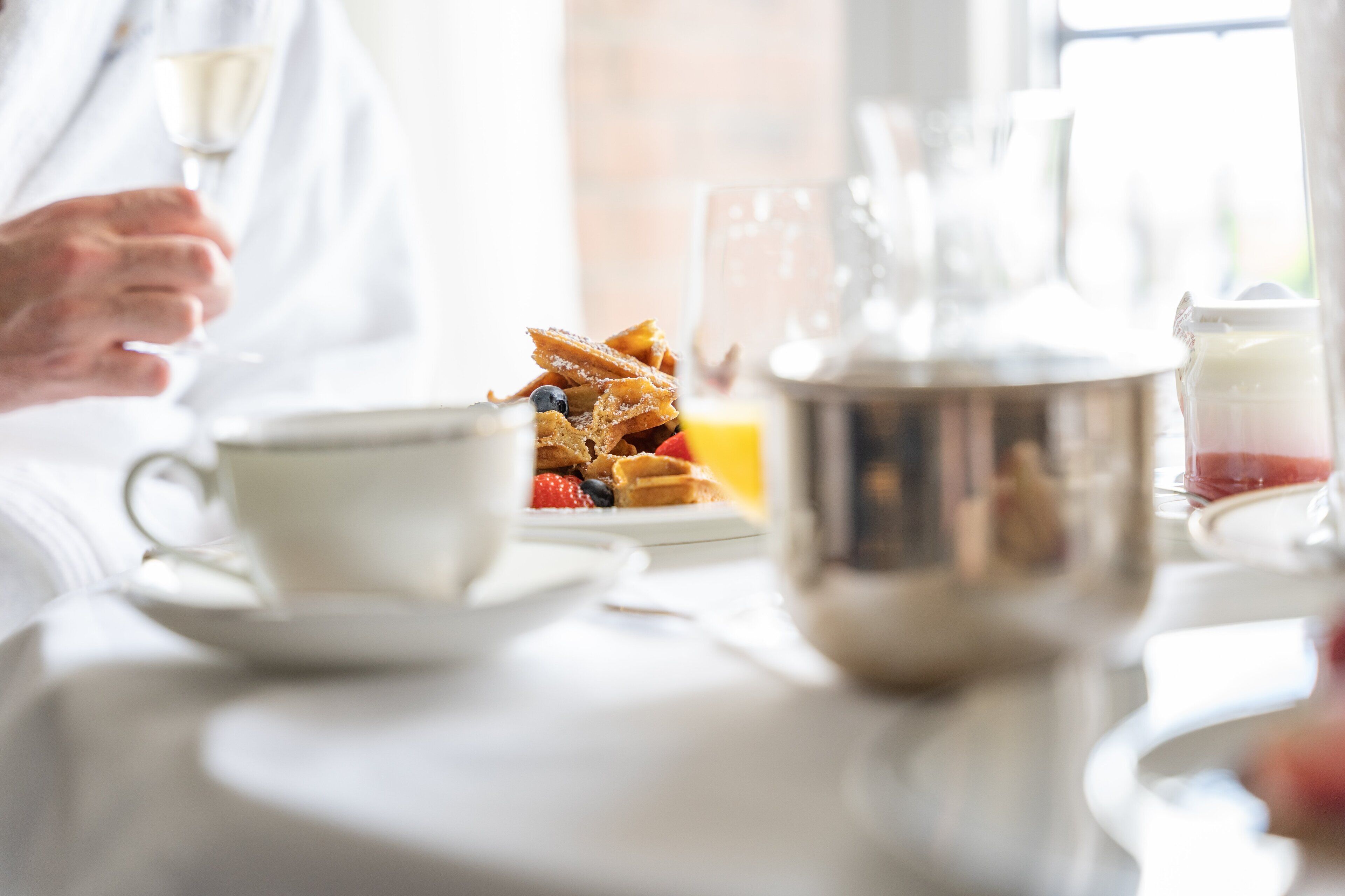 A breakfast setting with waffles, a cup, and a teapot on a table.