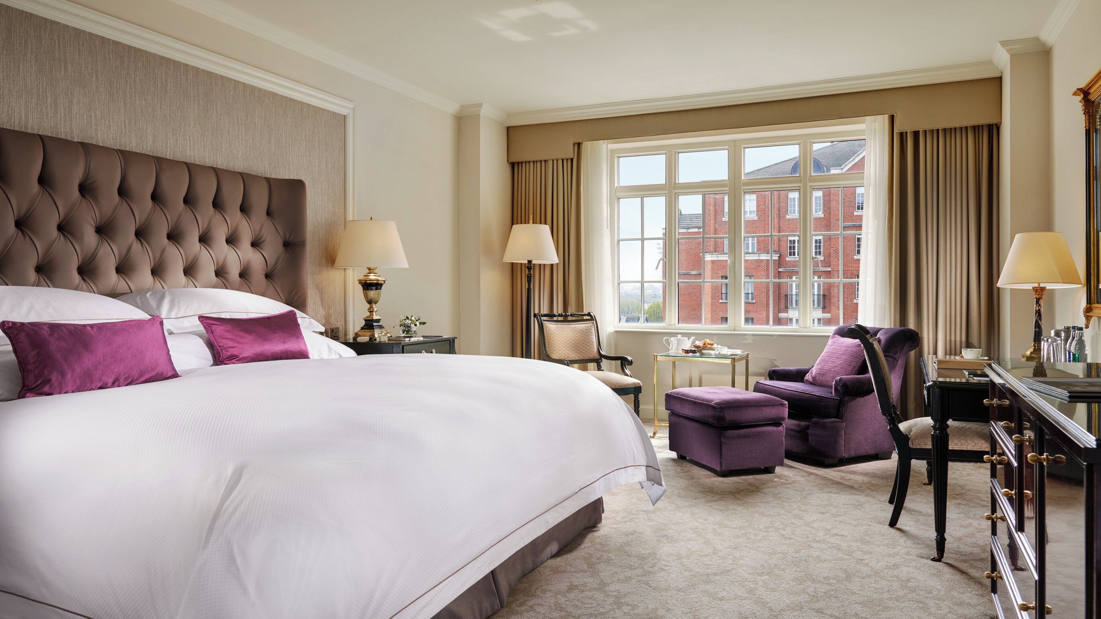 Une chambre d’hôtel avec un grand lit, deux fauteuils, un bureau et une fenêtre donnant sur des immeubles.