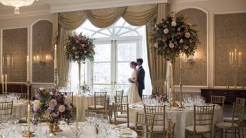 Uma recepção de casamento com mesas redondas, cadeiras douradas e centros de mesa florais.