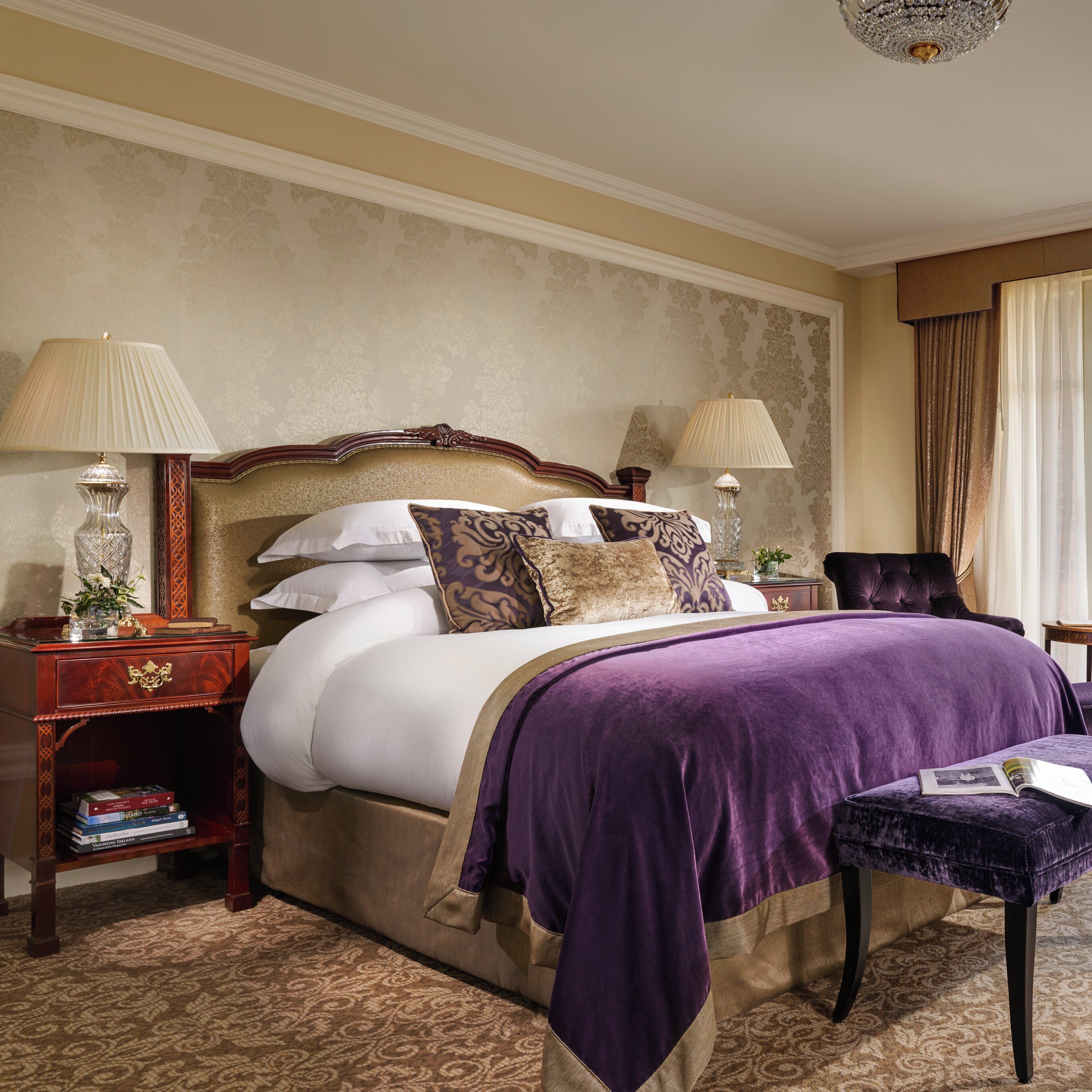 A hotel room with a large bed, two bedside tables, a nightstand, a chair, and a window with curtains.