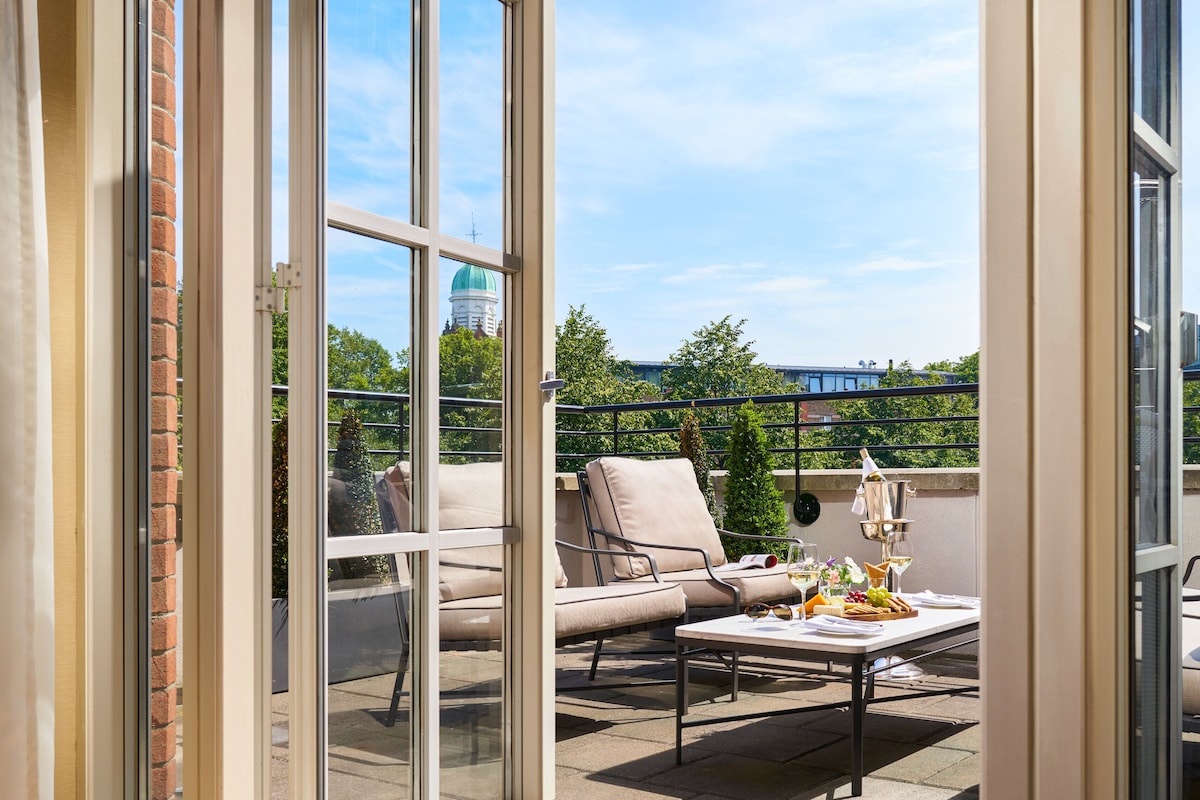 Un balcon avec un canapé, une table garnie de nourriture et de boissons, et une vue sur un bâtiment surmonté d’un dôme.
