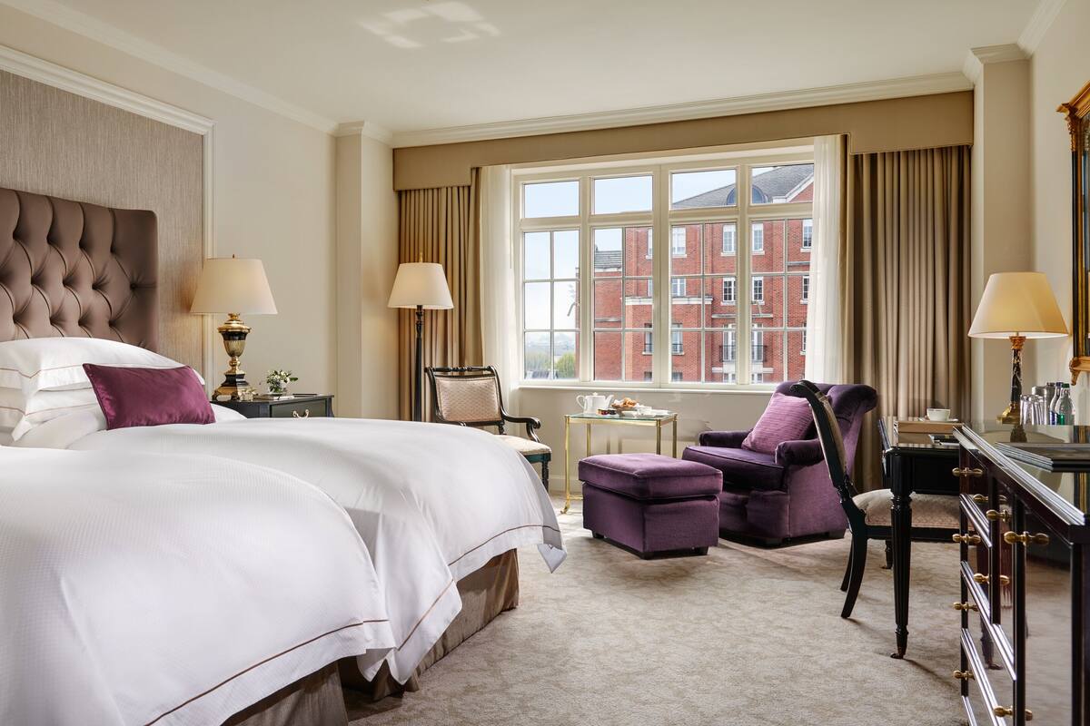 A hotel room with a large bed, two armchairs, a desk, and a view of a red brick building.