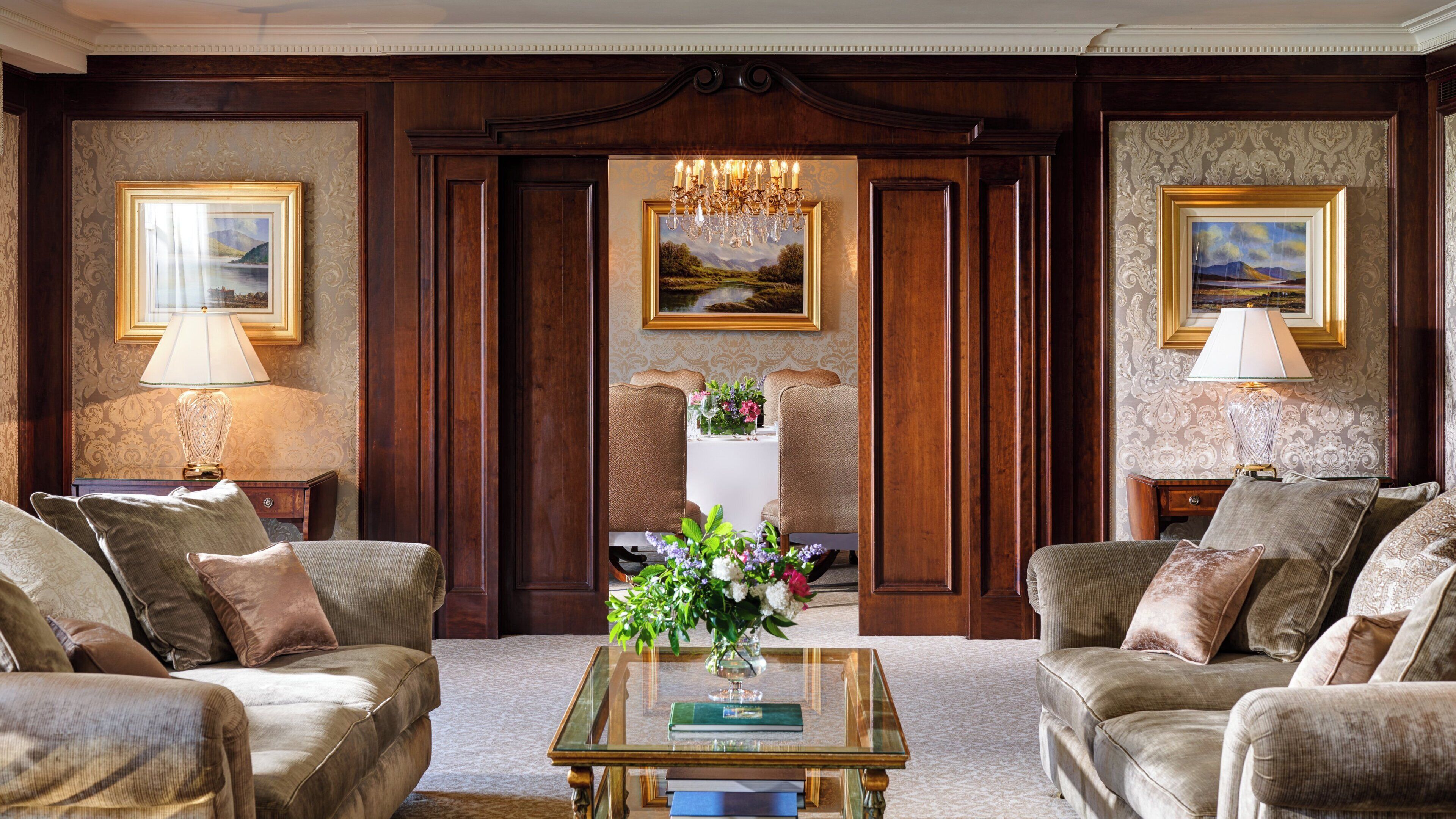 Un salón formal con dos sillones, una mesa de centro con un libro y flores, y dos lámparas.