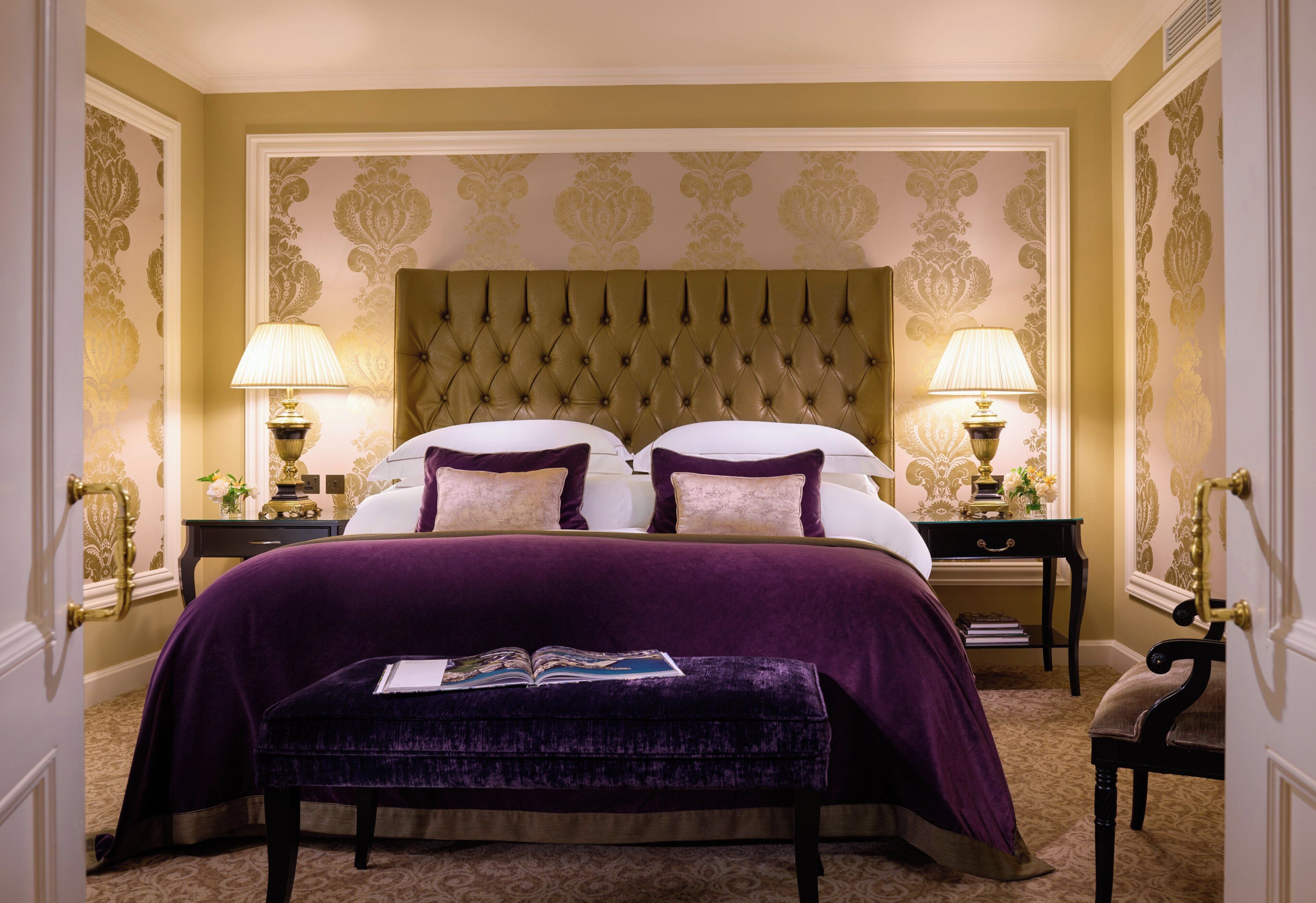A hotel room with a large bed, two bedside tables, a bench, and a decorative headboard.
