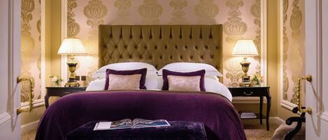 A hotel room with a large bed, two bedside tables, a bench, and a decorative headboard.