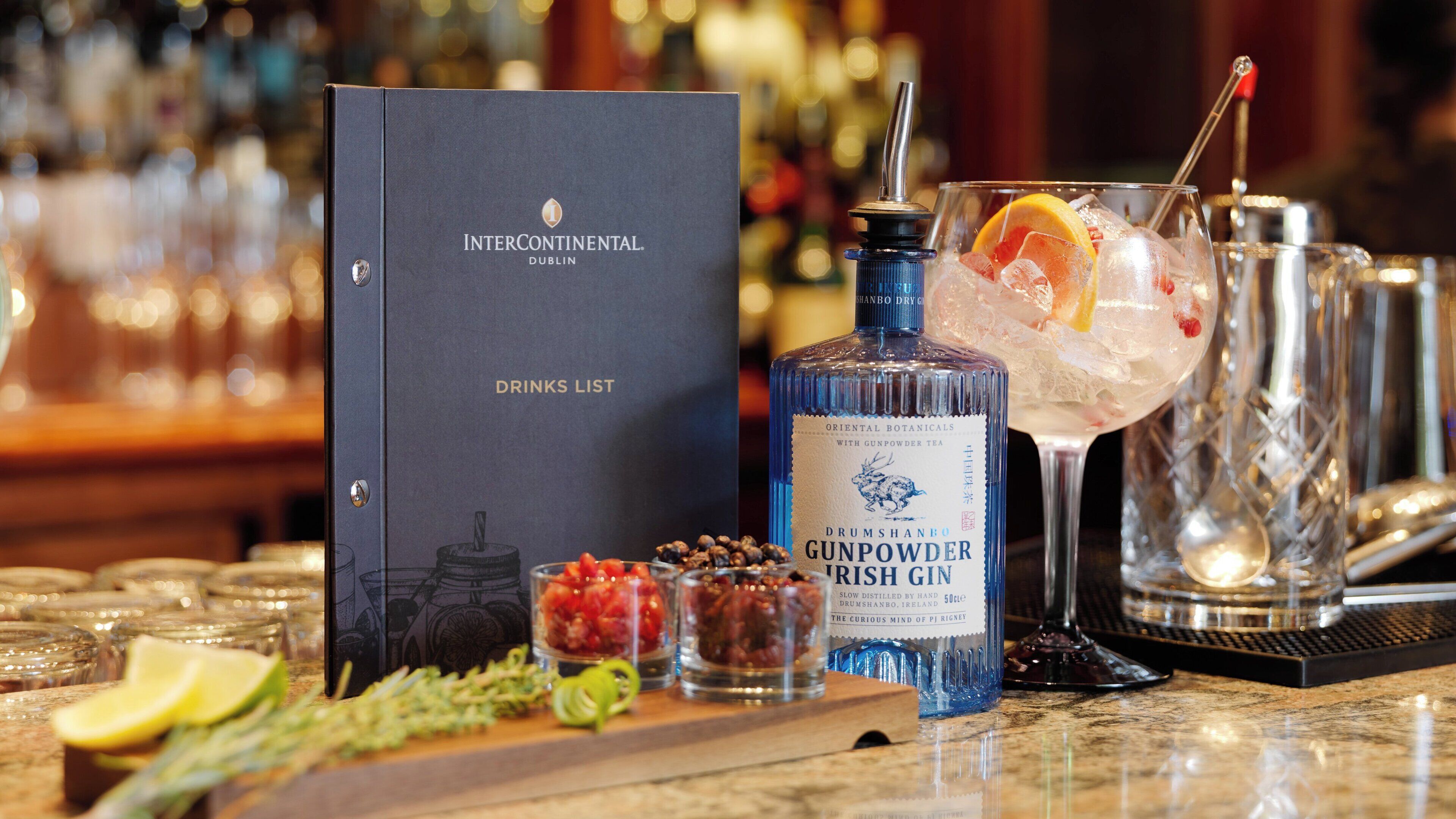 A bar setting with a drinks list, a bottle of gunpowder irish gin, and various garnishes.