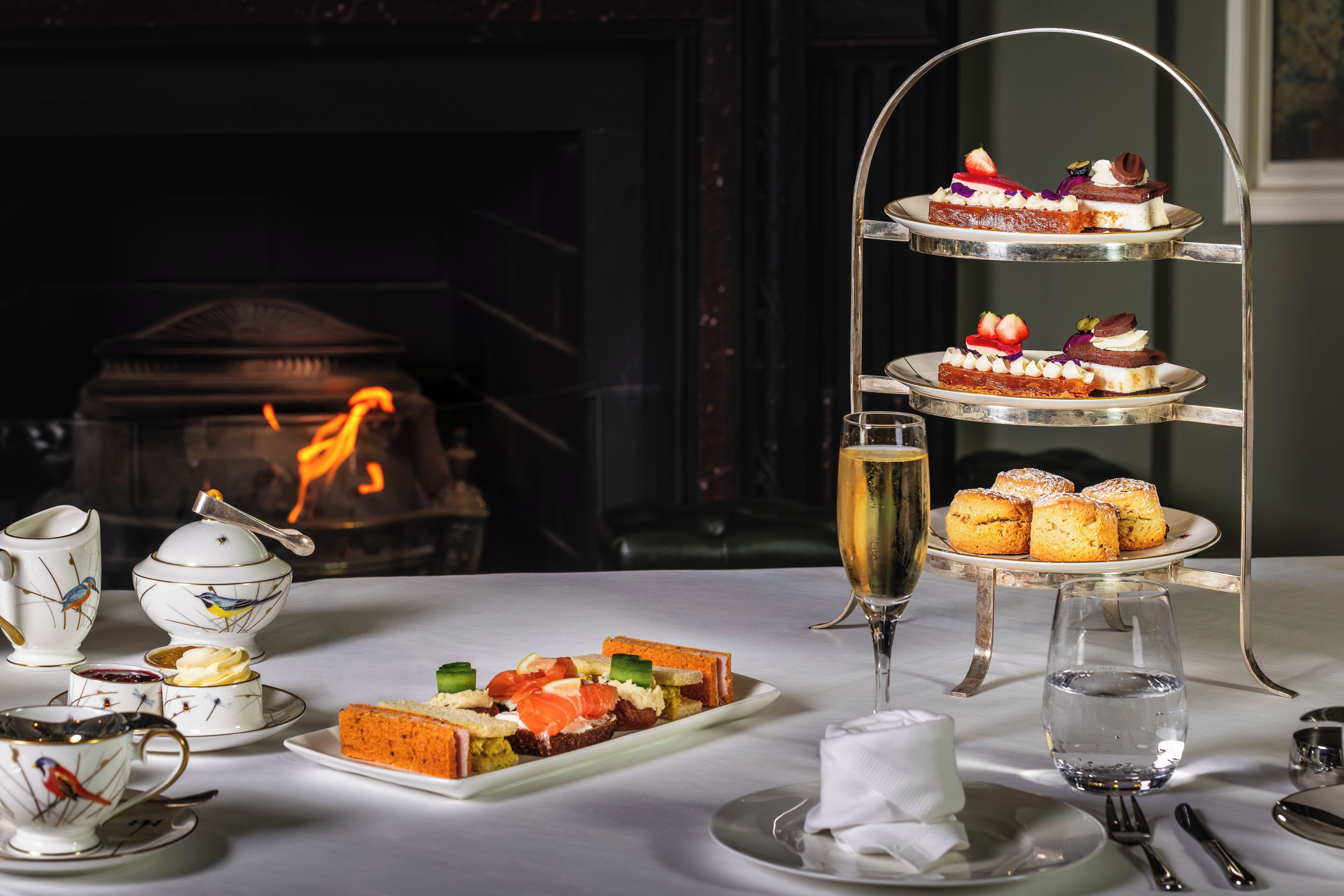 A three-tiered dessert stand with various pastries and a glass of champagne on a table.