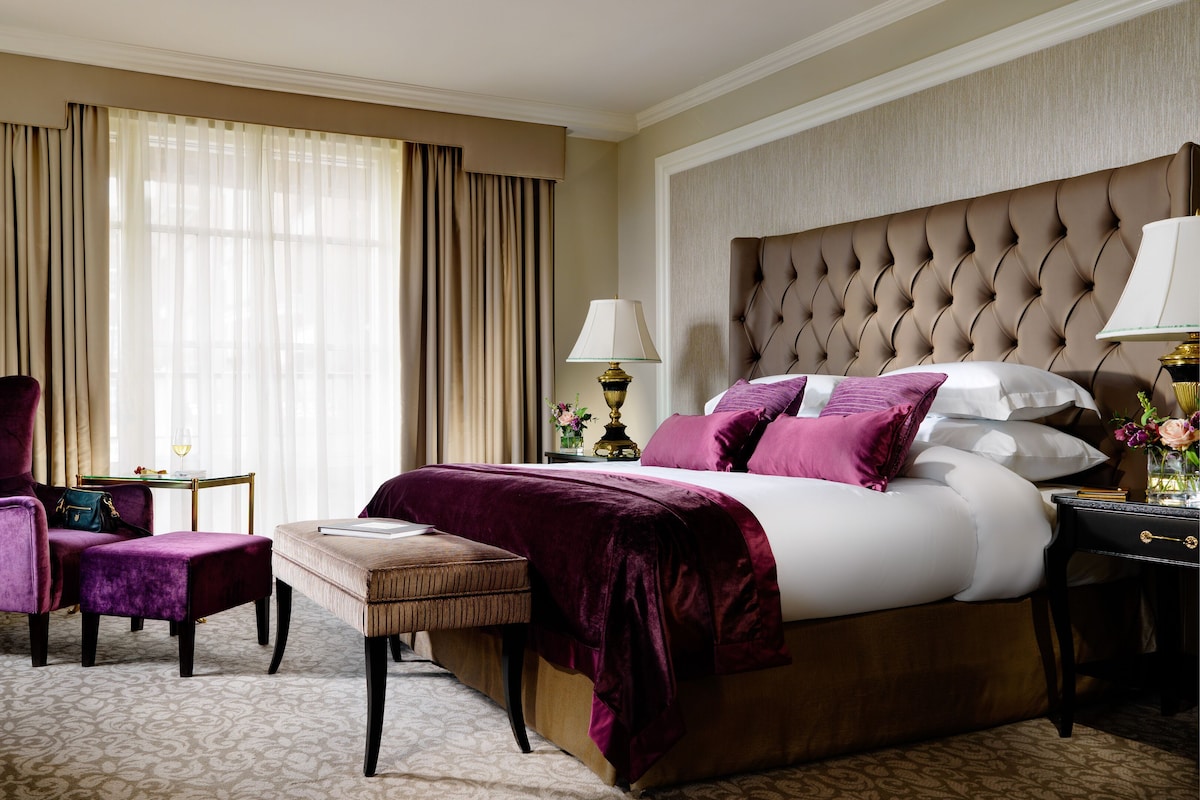 Une chambre d’hôtel avec un grand lit, une chaise, une petite table et une table de chevet avec des lampes.