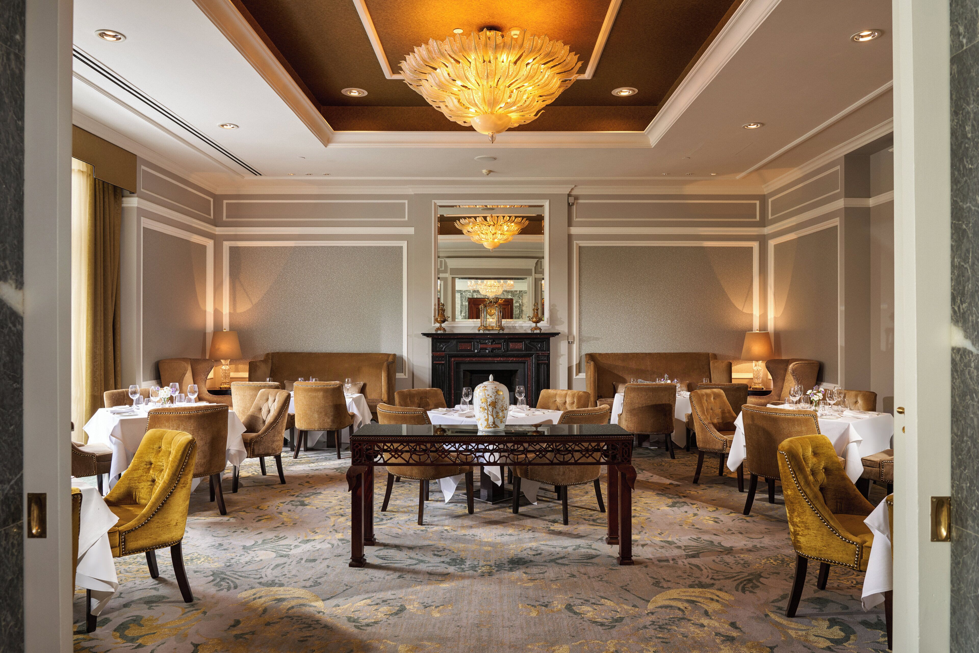 A formal dining room with a central table, surrounded by upholstered chairs, and a chandelier above.