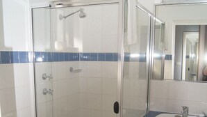 A bathroom with a glass-enclosed shower, a toilet, and a sink with a mirror above it.