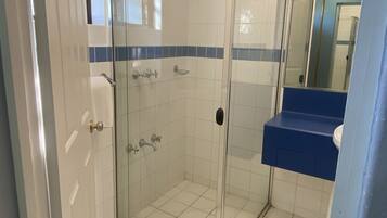 Une salle de bain avec une douche à parois de verre, un sol carrelé de blanc et un plan de toilette bleu.