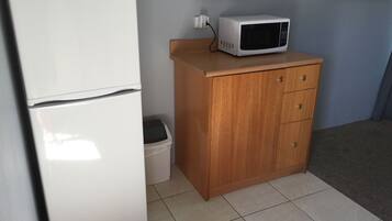 A compact kitchenette with a white refrigerator, a microwave, a wooden cabinet, and a trash bin.