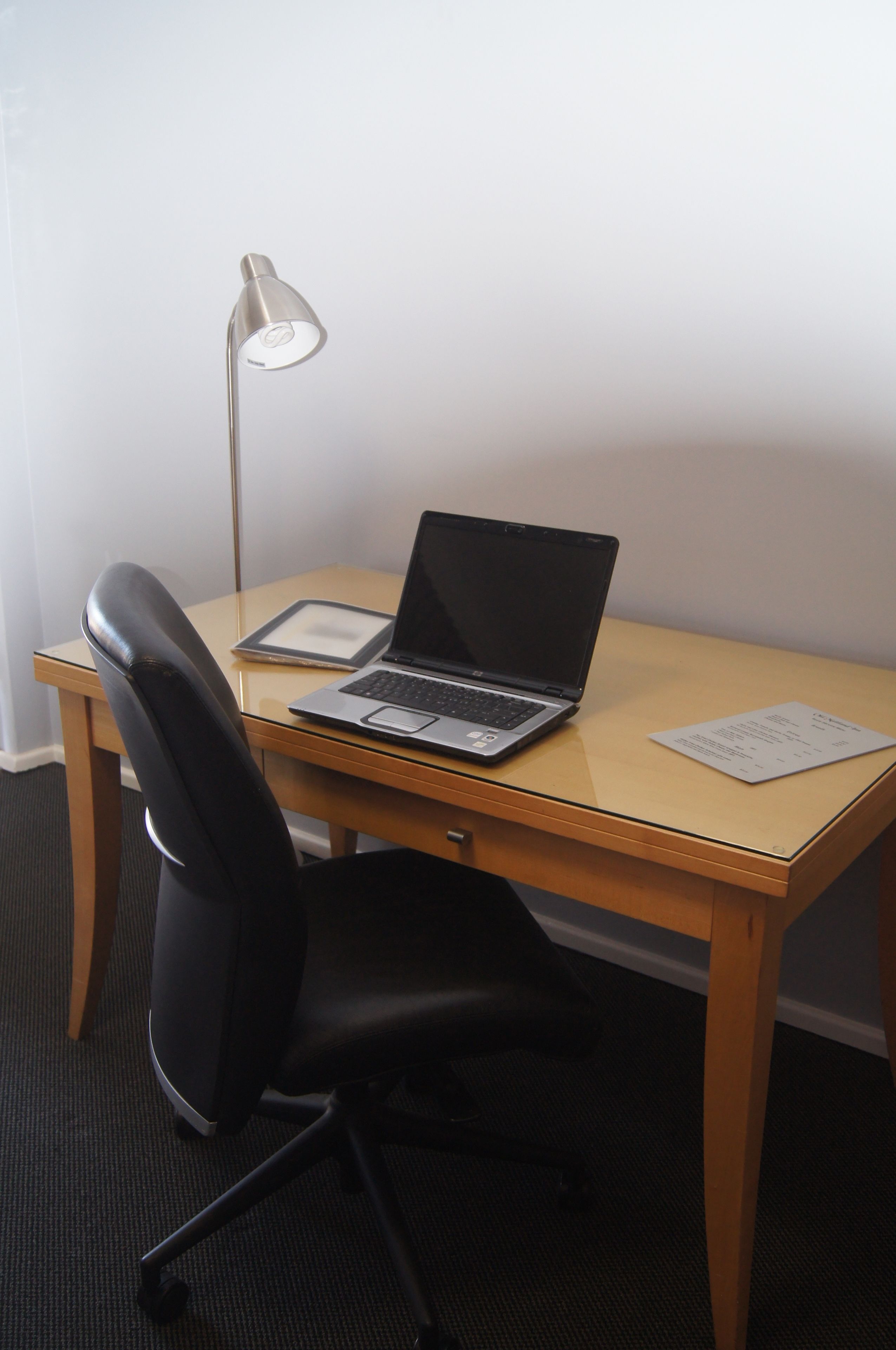 Un bureau en bois avec un ordinateur portable, une tablette et une lampe.