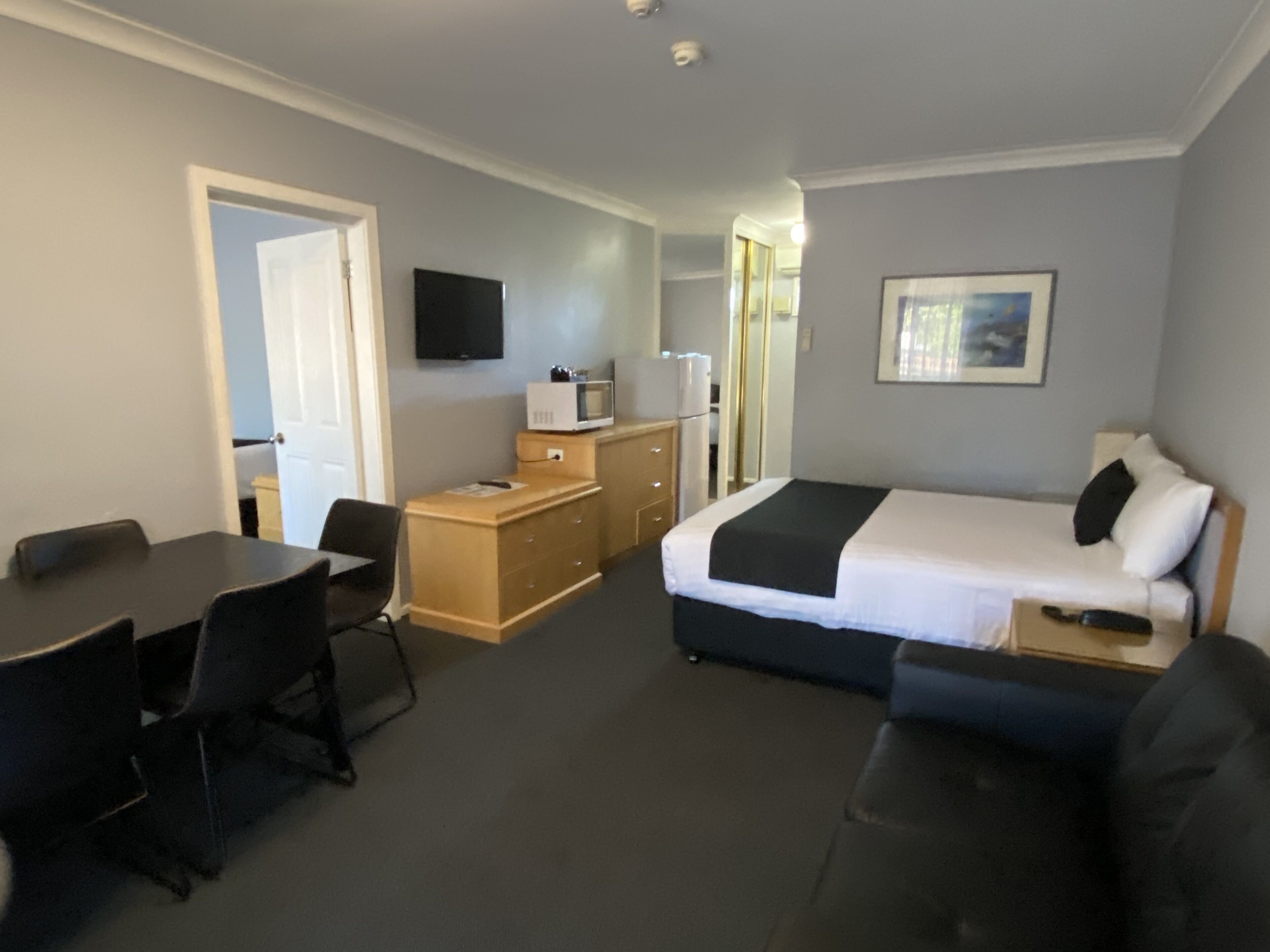 A compact hotel room with a bed, a desk, a chair, a television, and a door leading to another room.