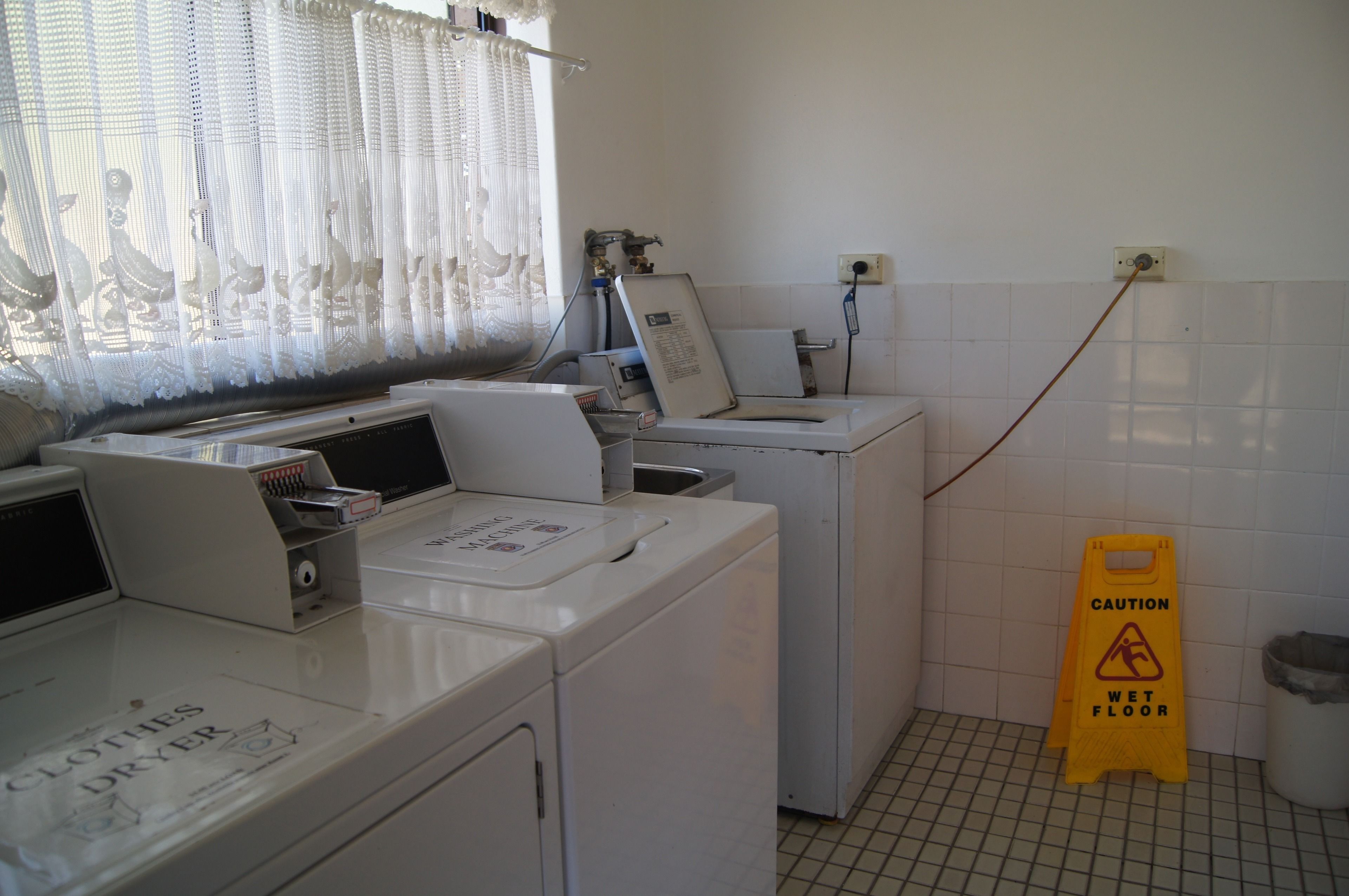 A laundry area with a clothes dryer, washing machine, and caution sign on a wet floor.