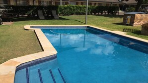 Una piscina rettangolare con piastrelle blu e superficie dell'acqua limpida, circondata da un'area erbosa e una struttura in mattoni.