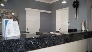Un'area reception con un bancone in marmo, una sveglia, un elemento decorativo a parete e un cartello informativo.
